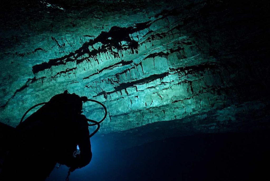 Grotta Grande della Ficarella, Riserva dello Zingaro (TP). Nel buio della cavità sommersa, le lampade degli speleologi subacquei fanno emergere la successione degli strati rocciosi: pagine di un archivio naturale che conserva, nelle sue forme e nelle sue fratture, milioni di anni di storia geologica della Sicilia e delle trasformazioni che hanno modellato questo tratto di costa mediterranea. Foto Vincenzo Sottosanti / Archivio LIMEN